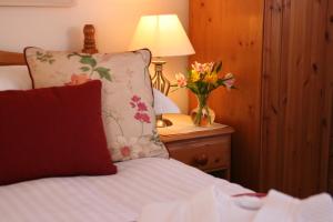 a bed with a pillow and a vase of flowers on a table at Mandeley Guest House in Helston