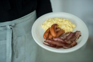 a person holding a plate of food with sausage and eggs at Pensionat Strandgården in Mölle