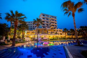 a hotel with a pool and palm trees at night at Aquamare Beach Hotel & Spa in Paphos