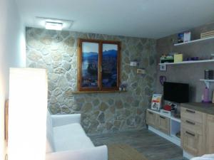 a living room with a stone wall with a couch and a television at Casetta next to the Creek Dino Buzzati in Belluno