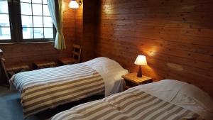 two beds in a room with wooden walls and windows at Pension Baden Heim in Nagasaki