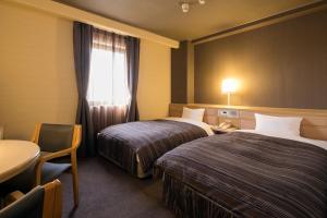 a hotel room with two beds and a table and a window at Ark Hotel Okayama -ROUTE INN HOTELS- in Okayama