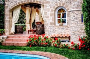 a stone house with a swimming pool and red flowers at Rock House's Villa Melody in Plataniás
