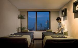 a man standing between two beds in a hotel room at Hotel Santika Pandegiling - Surabaya in Surabaya
