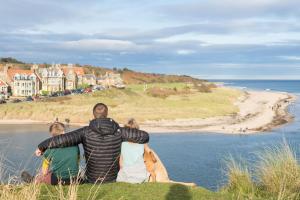 three people sitting on a hill looking at the beach at Estuary View Caravans in Alnmouth +10 photos