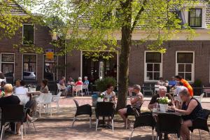 um grupo de pessoas sentadas em mesas debaixo de uma árvore em Herberg Swaen aan de Brink em Den Ham