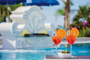 three glasses with orange slices in them on a table next to a pool at Hotel Capizzo in Ischia