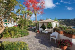 a patio with white chairs and an umbrella at Hotel Capizzo in Ischia