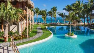 uma piscina de resort com palmeiras e o oceano em Zoetry Agua Punta Cana - All Inclusive em Punta Cana