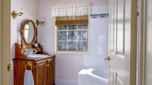 La salle de bains est pourvue d'un lavabo, d'un miroir et d'une baignoire. dans l'établissement Honeysuckle Cottages, à Stanthorpe