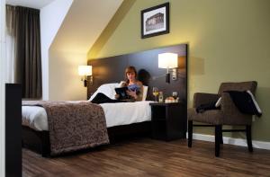 una mujer sentada en una cama en una habitación de hotel en Hotel De Maaskant en Maaseik