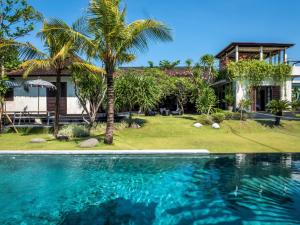 a house with a swimming pool and a palm tree at Holiday beautiful Villa 4 Bedroom Garden View Canggu in Canggu