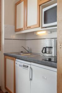 eine Küche mit weißen Schränken, einer Spüle und einer Mikrowelle in der Unterkunft Résidence Pierre & Vacances Emeraude in Belle Plagne