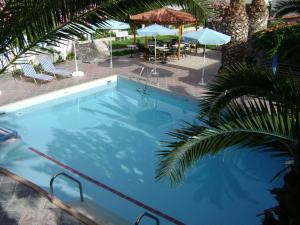a large blue swimming pool next to a patio with umbrellas at Chris Apartments in Marathokampos