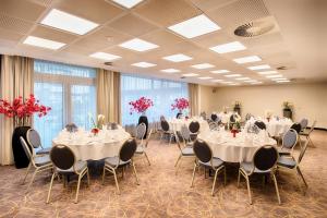einen Bankettsaal mit weißen Tischen, Stühlen und roten Blumen in der Unterkunft Leonardo Hotel Hamburg City Nord in Hamburg