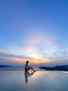 a person sitting in the water watching the sunset at Lilium Hotel Santorini in Fira