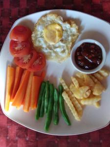 a plate of food with eggs and vegetables and french fries at Sunset Guest House & Bar in Bunaken