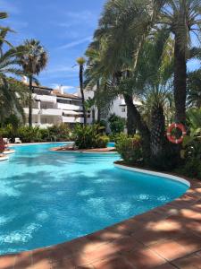 a swimming pool with palm trees and a building at Modern Apartment Puente Romano in Marbella