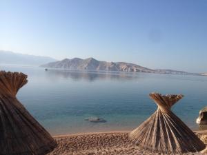 a view of the water from a beach with two straw umbrellas at Apartmani Srdoč in Baška