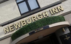 um sinal na frente de um edifício com um sinal de boas-vindas em Newburgh Inn em Ellon