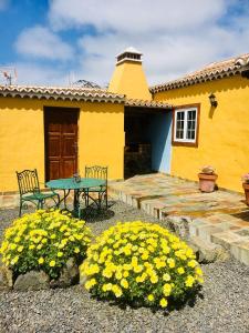 een geel huis met een tafel, stoelen en bloemen bij Casa Gusber 2 in La Rosa