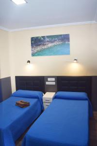 マドリードにあるオスタル ヌマンシアのブルーシーツ付きの客室内のベッド2台