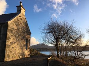 a building with a tree next to a body of water at Dunvegan Castle Keepers Cottage in Dunvegan