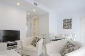 a white living room with two white chairs and a television at Entre Magnolios in Córdoba