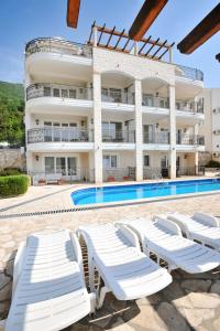 un bâtiment avec des chaises longues blanches et une piscine dans l'établissement Apartman ANNA Đenovići, à Herceg-Novi