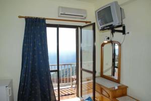 Zimmer mit einem Balkon, einem TV und einem Fenster in der Unterkunft Pansion Alexandros in Pelekas