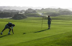 two people standing on a green golf course at Praia Del Rei Beach 3 Pools in Amoreira
