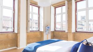a bedroom with windows and a bed with blue sheets at Praça 44 in Braga