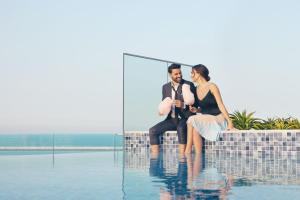 a man and a woman sitting next to a swimming pool at Mysk Al Mouj Hotel in Muscat