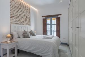 a white bedroom with a bed and a brick wall at Casas de Sevilla - Apartamentos Tintes12 in Seville