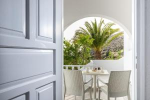 een witte deur met stoelen en een tafel en een palmboom bij Nostos in Matala