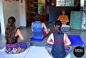 a group of three girls sitting on the floor watching a man at Social Hostel Café e Bar in Curitiba