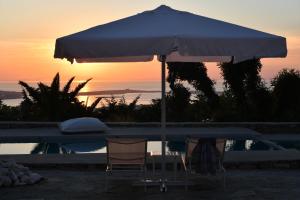un tavolo e due sedie sotto un ombrellone accanto a una piscina di Paros Butterfly Villas a Pounda