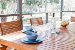 a wooden table with a bottle of wine and bowls of fruit at McLean Beach Holiday Park in Deniliquin