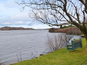 un banco verde sentado junto a un cuerpo de agua en The Lake House, Connemara en Knock