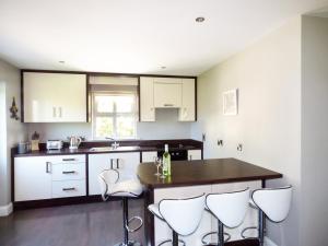 una cocina con armarios blancos, mesa y taburetes en Hidden Gem Cottage, en Dungloe