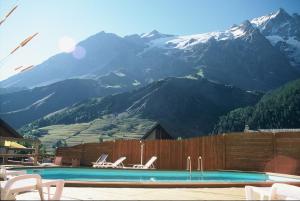 a swimming pool with chairs and mountains in the background at Chez Philippe - Appartements et Chalets - Panoramic Village vue Glaciers in La Grave +62 photos