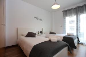 two beds in a bedroom with white walls and windows at Surf and Stones Apartment in Peniche