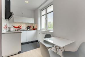 グディニャにあるGdynia Comfort Apartments Władysława IVの白いキャビネット、テーブルと椅子付きのキッチンが備わります。