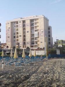 eine Gruppe von Stühlen und Sonnenschirmen an einem Strand mit einem Gebäude in der Unterkunft Quartz Apartament in Durrës
