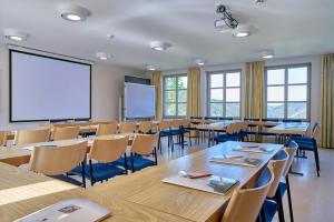 バート・ミュンスター・アム・シュタイン・エーベルンブルクにあるEv.Familienferien-und Bildungsstätte Ebernburgのテーブルと椅子、プロジェクションスクリーン付きの教室