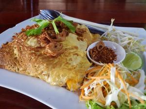 a white plate of food with a omelet and noodles at Pine Bungalow Krabi in Klong Muang Beach
