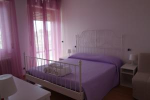 a bedroom with a white bed with purple sheets and windows at B&B Verderosa in Cupra Marittima