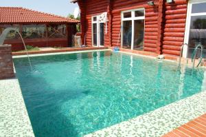 a swimming pool in front of a wooden house at Rönk-wellness Panzió Mezőpeterd in Mezőpeterd