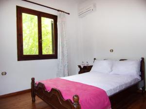 1 dormitorio con 1 cama con manta rosa y ventana en Vaso's Bay House, en Yénion