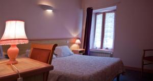 a bedroom with a bed and a table with a lamp at Hotel De La Poste in Saint-Martin-sous-Vigouroux